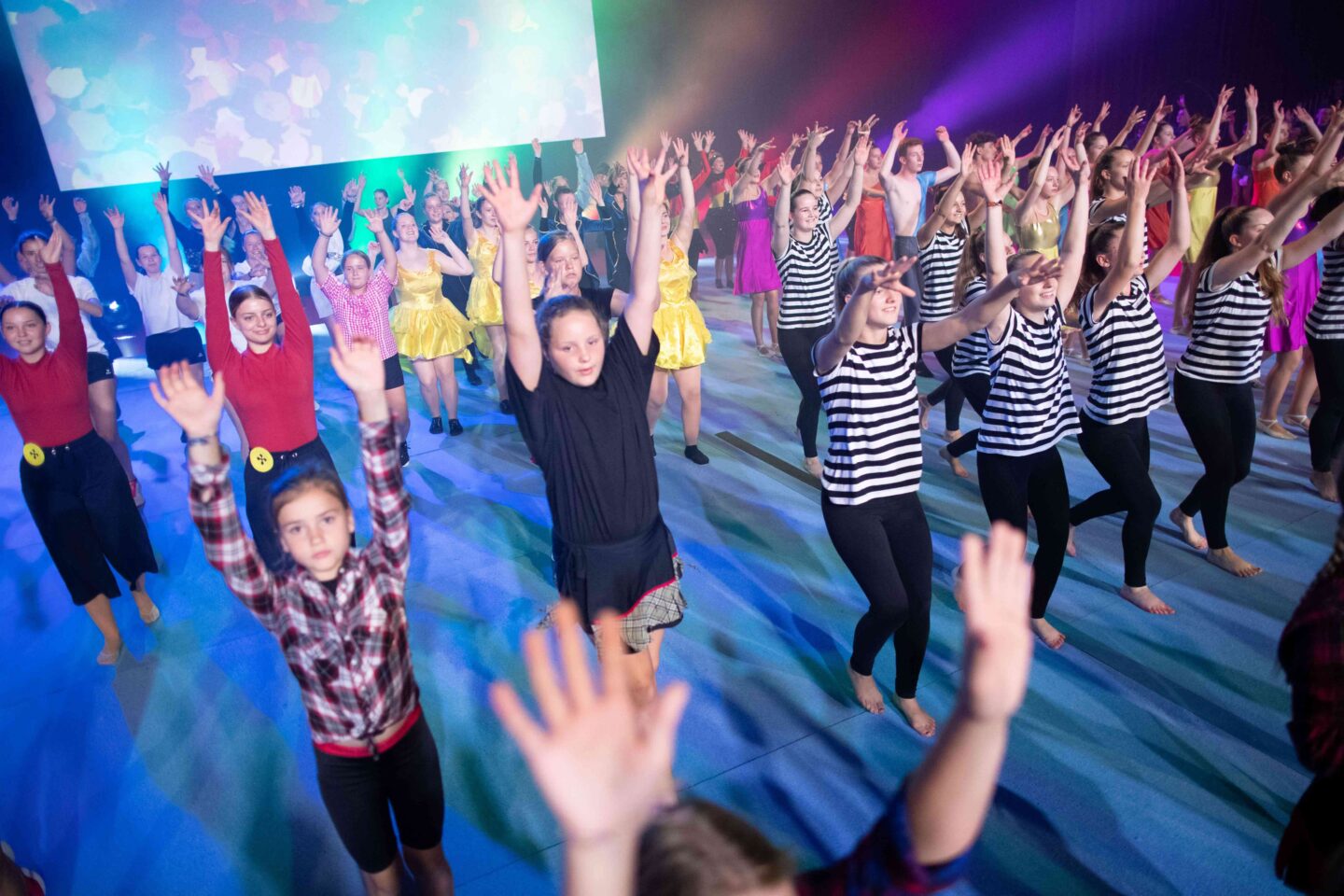 Tanzende Gruppe von Mädchen und Frauen mit erhobenen Händen auf einer Bühne.
