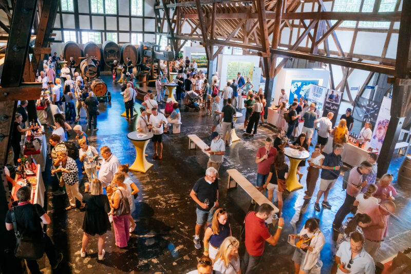 Menschenmenge bei einer Veranstaltung in einer großen Halle mit Holzstruktur.