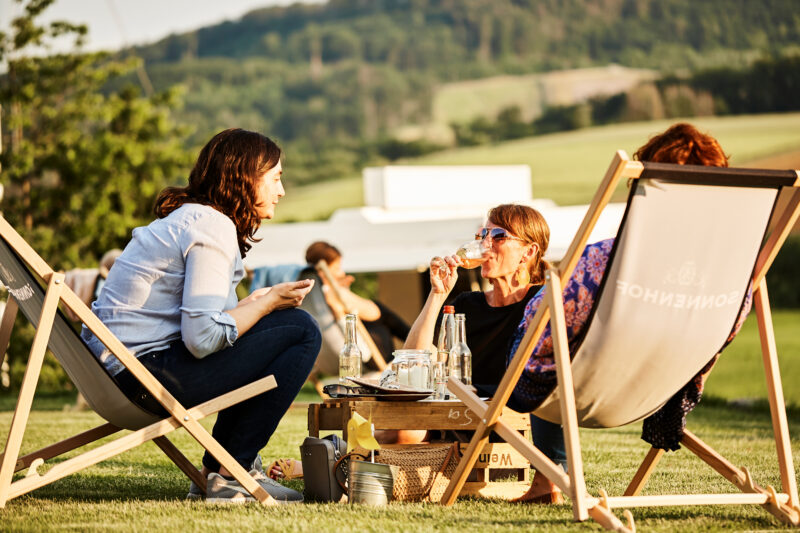 Drei Frauen entspannen im Freien mit Getränken und Snacks.