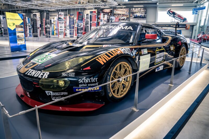 Schwarzes Rennfahrzeug mit goldenen Felgen in einem Ausstellungsraum.