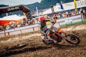 Motocrossfahrer auf einer Strecke mit Zuschauern im Hintergrund.