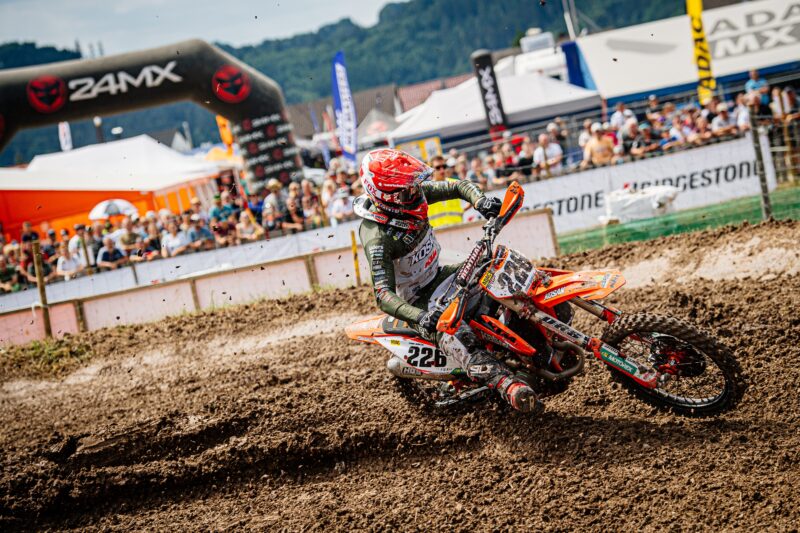 Motocrossfahrer auf einer Strecke mit Zuschauern im Hintergrund.