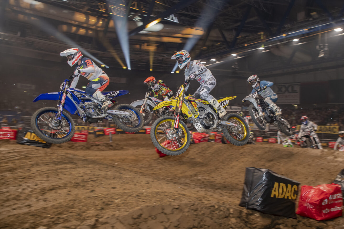 Motocross-Rennfahrer springen über eine Strecke in einer Halle.