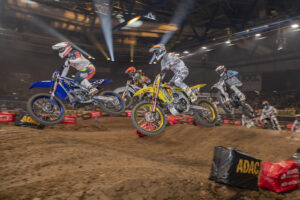 Motocross-Rennfahrer springen über eine Strecke in einer Halle.