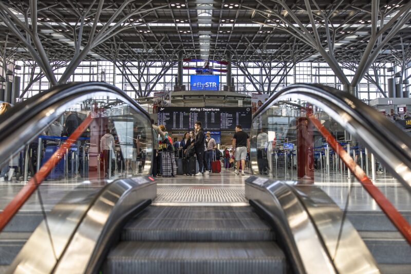 Blick auf einen modernen Flughafen mit Reisenden und Abflugtafel.