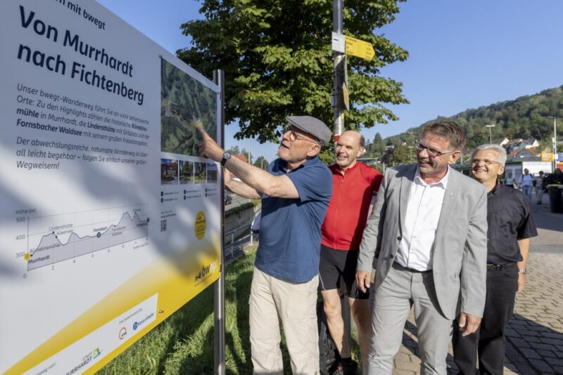 Gruppe von Männern betrachtet ein Informationsschild über Wanderwege.