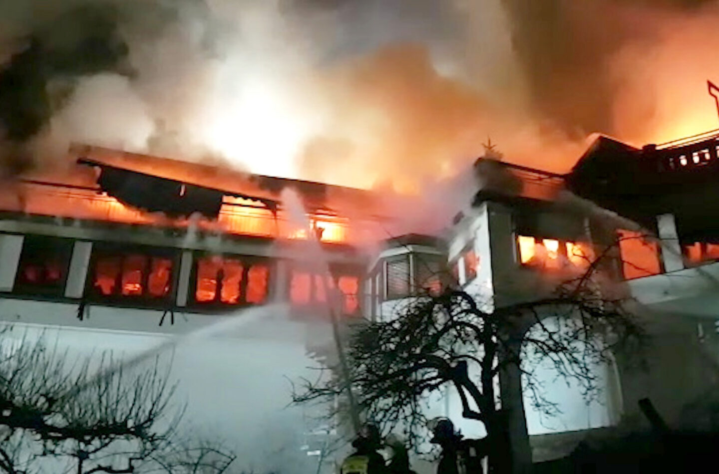Feuerwehrleute bekämpfen ein großes Feuer in einem Gebäude bei Nacht.