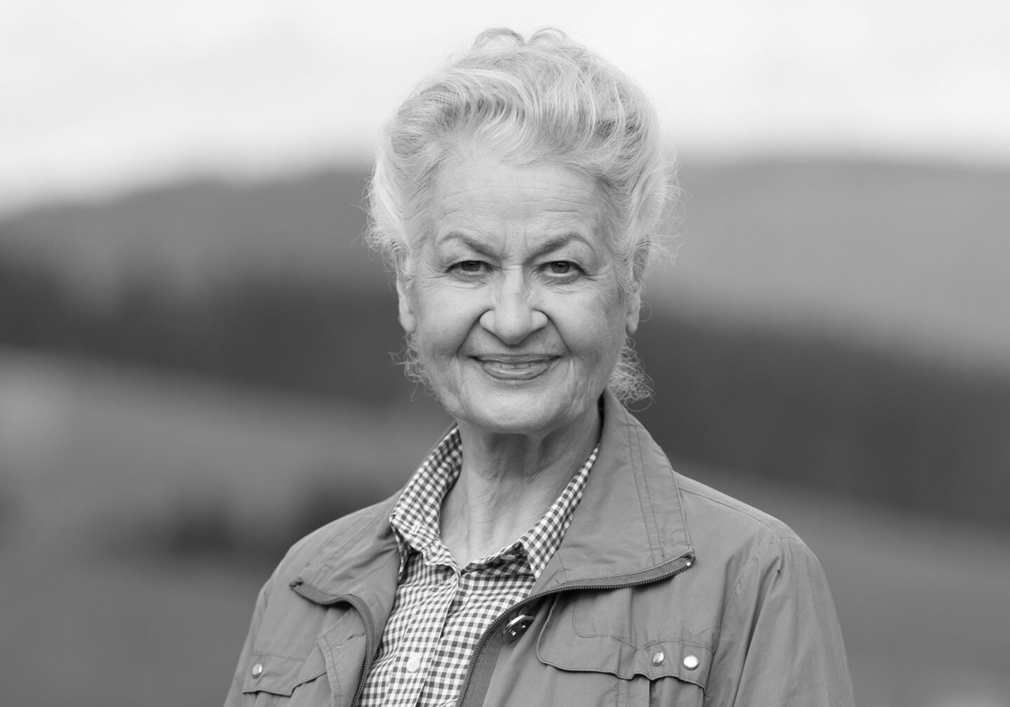 Ältere Frau mit grauen Haaren und freundlichem Lächeln im Freien.