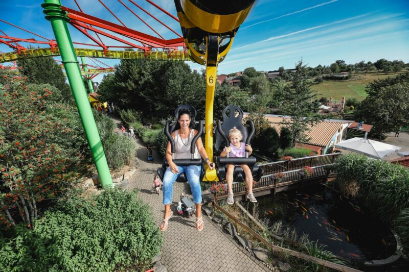 Frau und Kind in einer Gondelbahn über einem Freizeitpark.