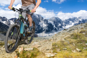 Mann fährt Mountainbike in den Bergen mit schneebedeckten Gipfeln im Hintergrund.