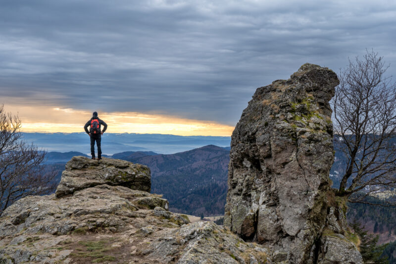 Wanderer steht auf einem Felsen mit Blick auf die Berge und den Sonnenuntergang.