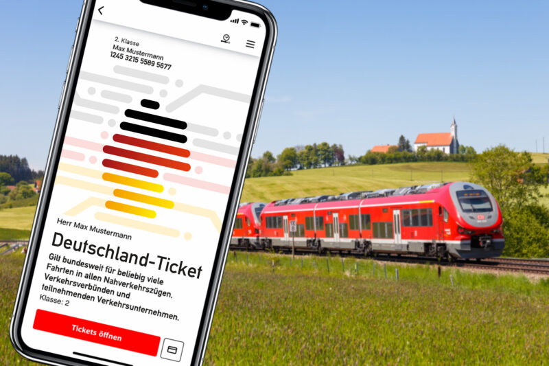 Smartphone zeigt Deutschland-Ticket vor einem Zug in ländlicher Umgebung.