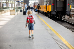 Ein Junge mit einem roten Rucksack geht am Bahnhof entlang.