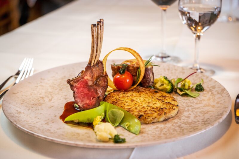 Ein kunstvoll angerichteter Teller mit Lammkoteletts, Gemüse und Beilagen.