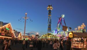 Bunt erleuchtetes Volksfest mit Fahrgeschäften und Menschenmengen bei Dämmerung.