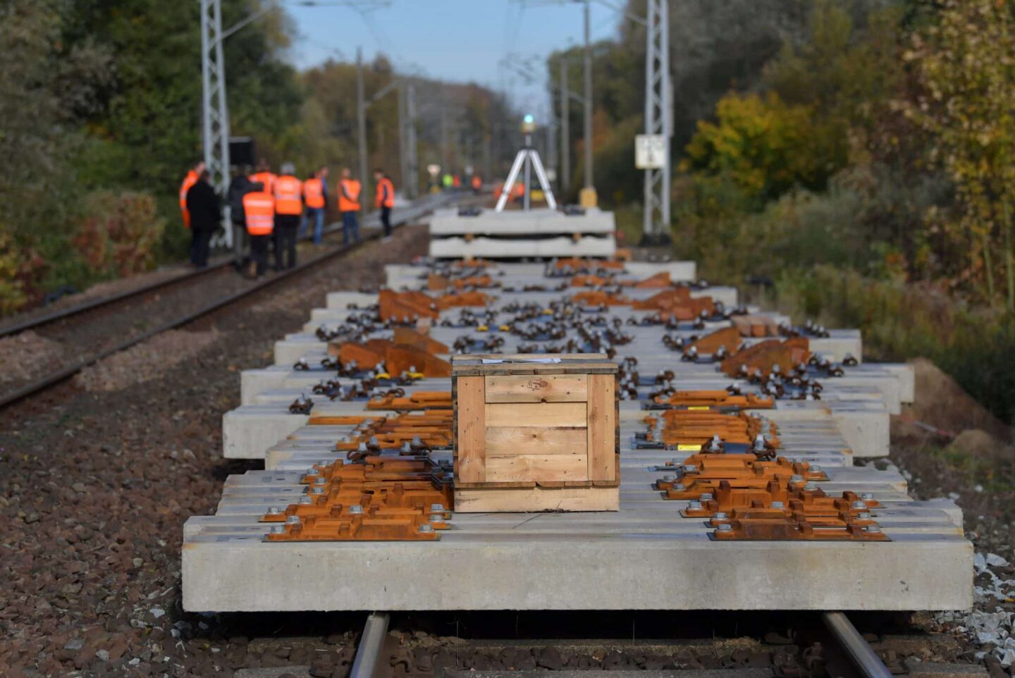 Bauarbeiten an Gleisen mit Holzbox und Arbeitern in Warnwesten im Hintergrund.