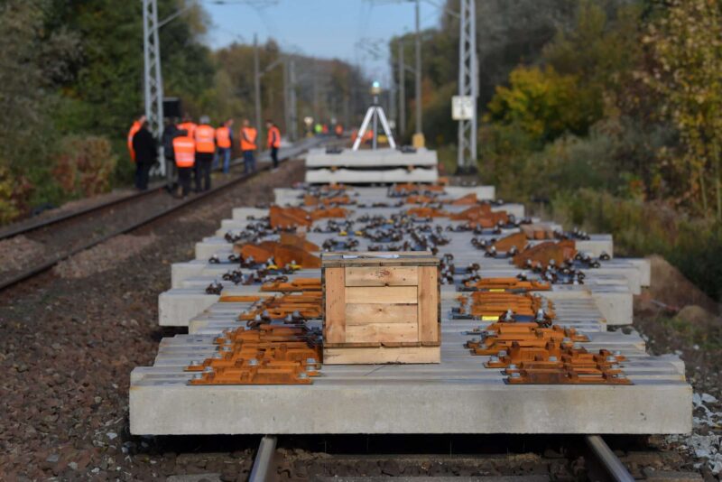 Bauarbeiten an Gleisen mit Holzbox und Arbeitern in Warnwesten im Hintergrund.