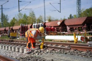 Arbeiter in Warnkleidung arbeitet an Gleisen mit Werkzeug.