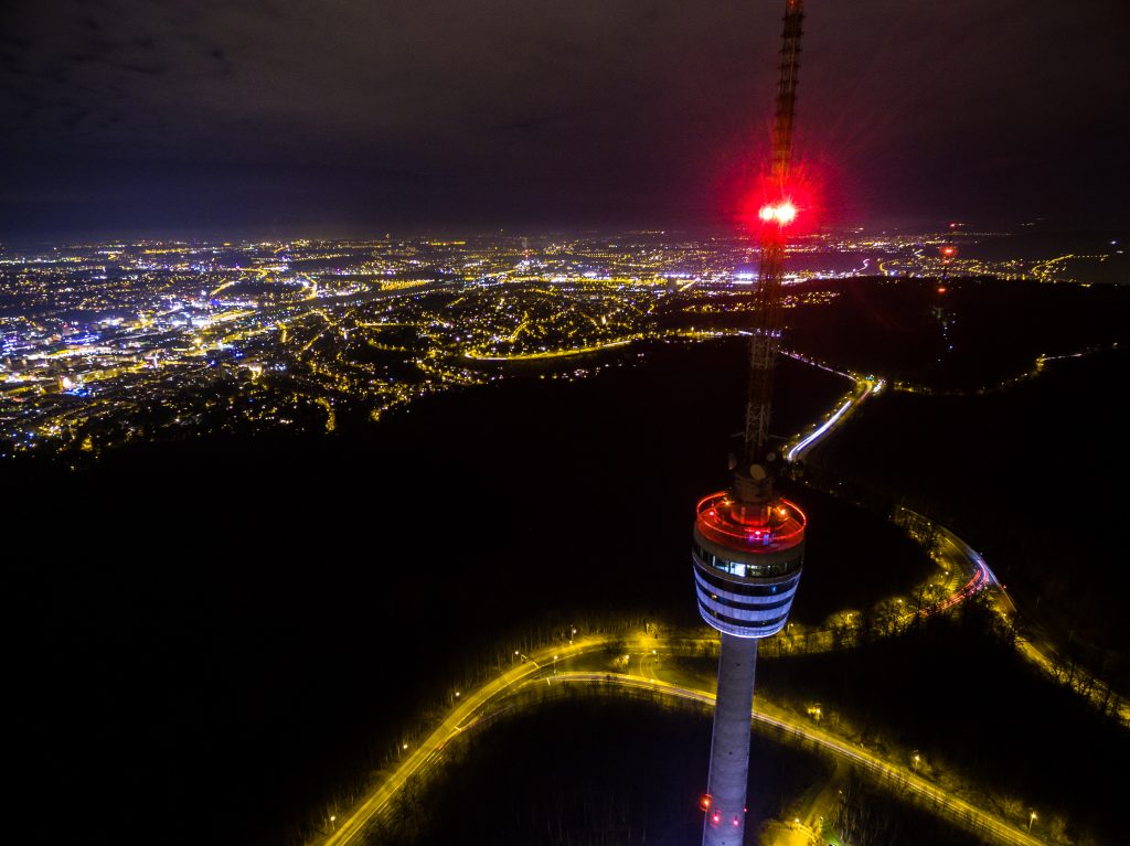 Fernsehturm und Antenne bei Nacht, im Hintergrund die Stuttgarter Innenstadt
