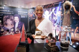 Frau in eleganter Kleidung hält einen Grammy-Award in einer festlichen Umgebung.