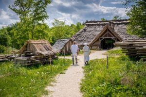 Zwei Personen gehen einen Weg zu einem historischen Gebäude in der Natur.