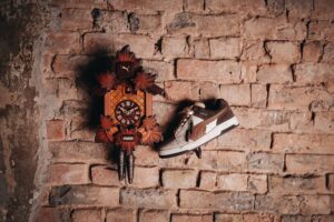 Ein Schuh hängt neben einer traditionellen Kuckucksuhr an einer Ziegelwand.