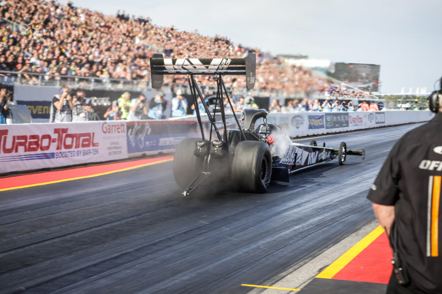 Dragster beschleunigt auf der Rennstrecke mit Zuschauermenge im Hintergrund.