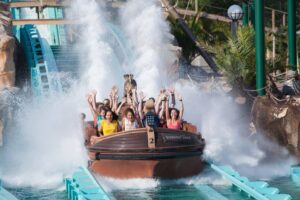 Gruppe von Menschen in einer Wasserbahn, die Freude zeigt und Wasser spritzt.