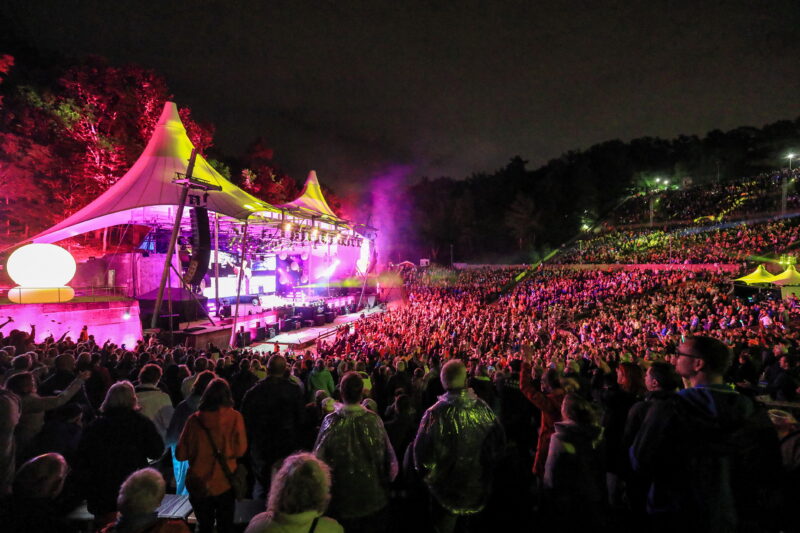 Großes Konzert mit vielen Menschen unter bunten Lichtern bei Nacht.