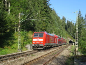 Rote DB-Zug fährt in einen Tunnel, umgeben von Wald.