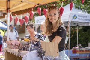 Junge Frau lächelt am Marktstand mit Dekoration und Produkten.