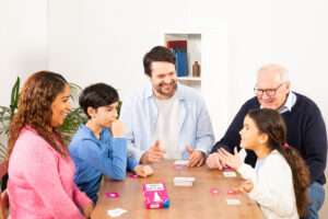 Familie spielt ein Kartenspiel am Tisch in einem hellen Raum.
