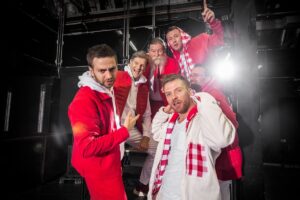 Sechs Männer in roten und weißen Outfits posieren fröhlich in einem Studio.