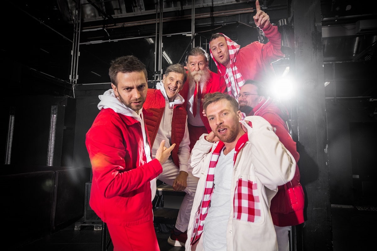 Sechs Männer in roten und weißen Outfits posieren fröhlich in einem Studio.