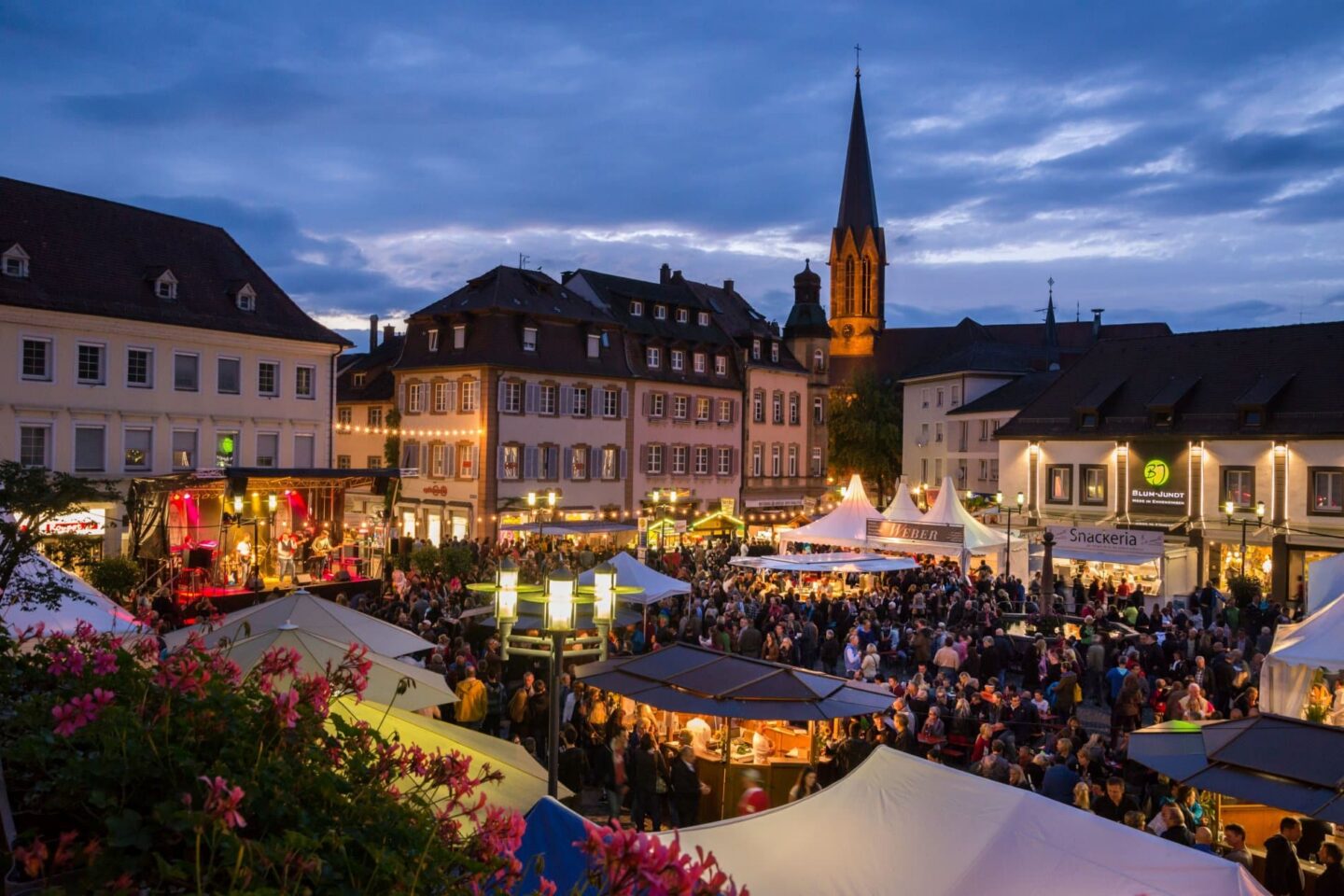Belebter Marktplatz bei Nacht mit vielen Menschen und Ständen.