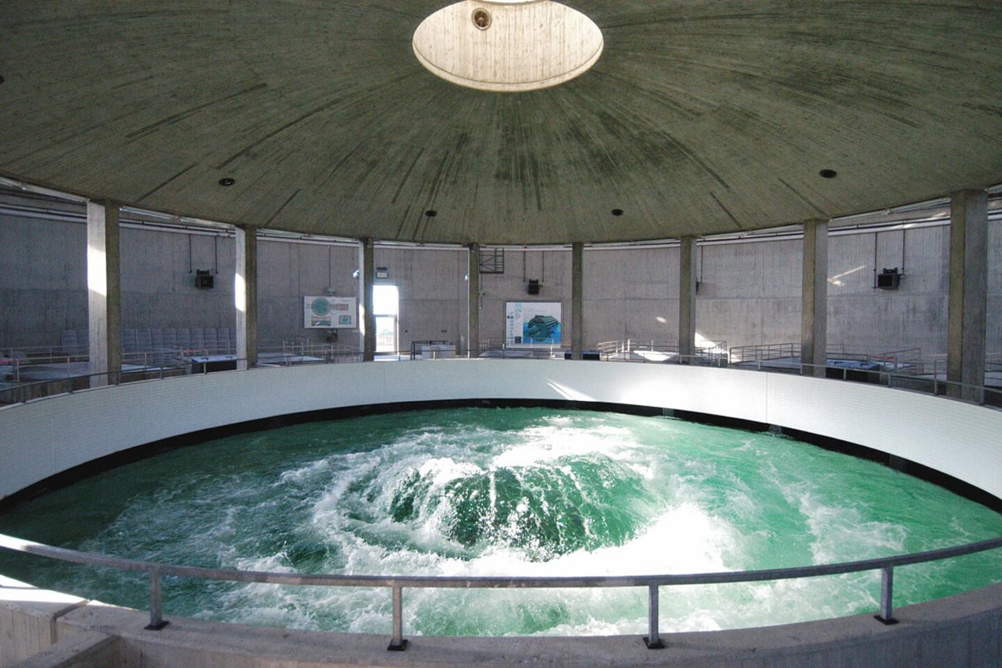 Runder Wassertank mit grünem Wasser und kreisförmiger Umrandung in einem modernen Gebäude.