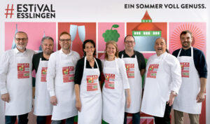 Gruppe von Menschen in Kochschürzen vor einem bunten Hintergrund.