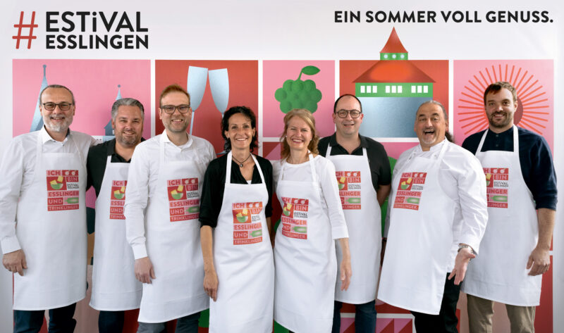 Gruppe von Menschen in Kochschürzen vor einem bunten Hintergrund.