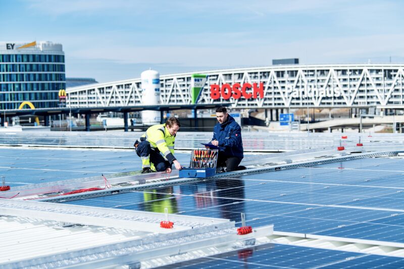 Zwei Techniker arbeiten auf einem Dach mit Solarpanelen.