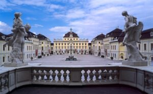 Blick auf ein Schloss mit Skulpturen im Vordergrund und blauem Himmel.