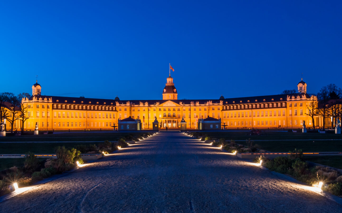 Beleuchtetes Schloss bei Nacht mit Garten und Weg.