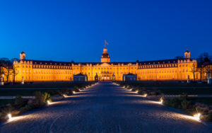 Beleuchtetes Schloss bei Nacht mit Garten und Weg.