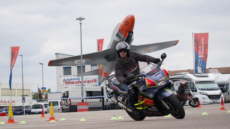 Mann auf Motorrad fährt durch einen Parcours mit einem Flugzeug im Hintergrund.