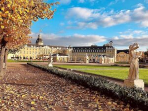 Herbstliche Parklandschaft mit Skulpturen und historischem Gebäude im Hintergrund.