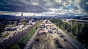 Bauarbeiten an einer Bahnstrecke mit Baustellenfahrzeugen und Wolken am Himmel.