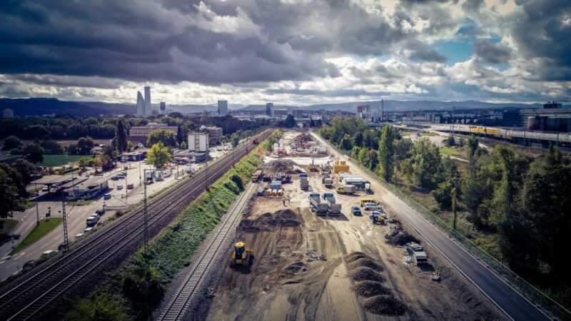 Bauarbeiten an einer Bahnstrecke mit Baustellenfahrzeugen und Wolken am Himmel.