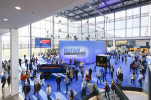 Menschenmenge auf der NUFAM Nutzfahrzeugmesse mit Ausstellungsständen und einem Lkw.