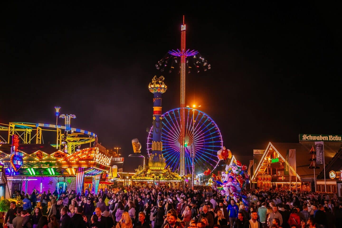 Bunt erleuchtetes Volksfest mit Fahrgeschäften und Menschenmenge bei Nacht.