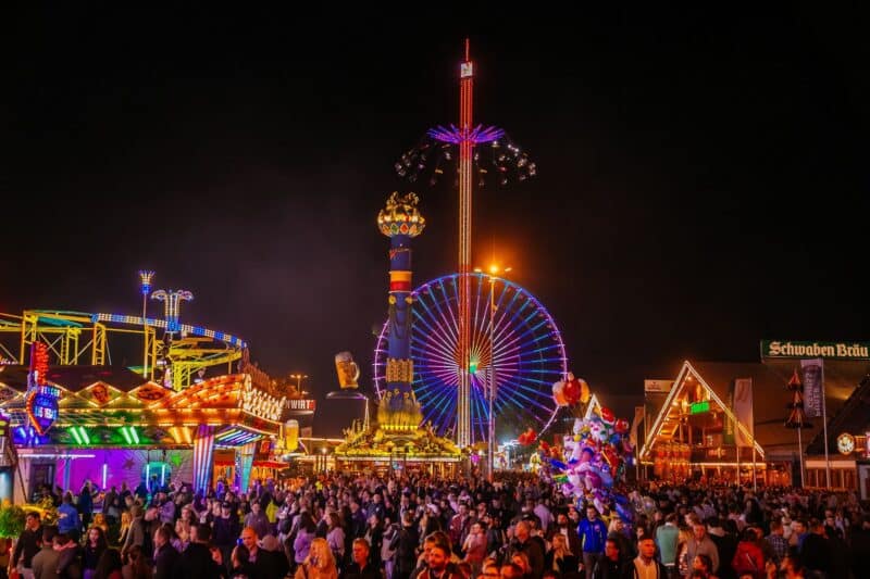 Bunt erleuchtetes Volksfest mit Fahrgeschäften und Menschenmenge bei Nacht.