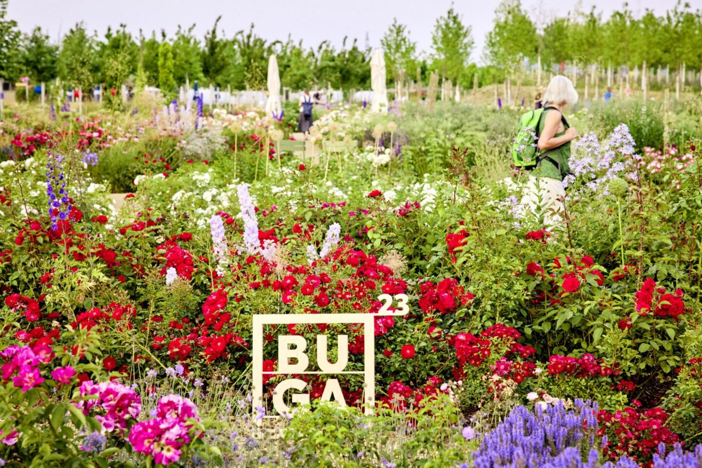 Frau mit Rucksack in einem blühenden Garten voller Blumen.